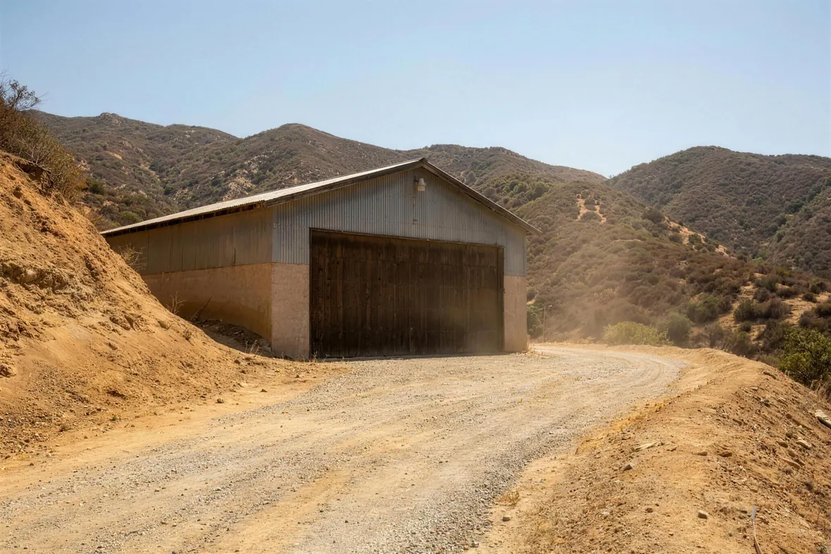 A large detached garage on a dusty canyon lot below scrub-covered ridges