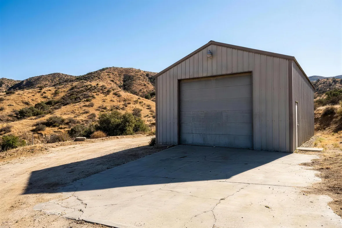 An oversized garage door on a detached workshop below dry hills
